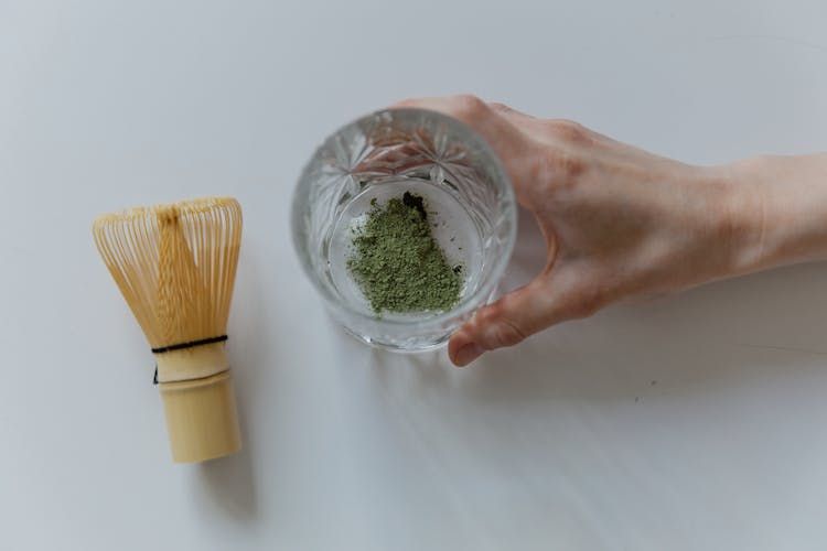 Elegant top view of matcha powder preparation with a bamboo whisk and hand holding glass.